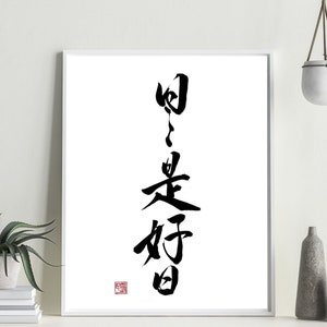 以下が含まれることがあります： 「日々是好日」 (hibi wa kōjitsu) と書かれた白黒の書道アートプリント。これは「毎日が良い日」という意味です。プリントは白いフレームに額装され、左下の隅に赤い印があります。