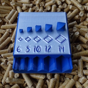 May include: A blue and white 3D-printed tool with various geometric shapes and the numbers 6, 8, 10, 12, and 14. The tool features square and diamond shapes of increasing sizes. The tool is resting on a bed of wood pellets.