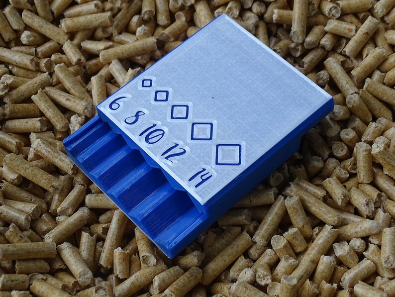 May include: A blue and white plastic container with a sliding tray, featuring the numbers 6, 8, 10, 12, and 14, along with diamond-shaped symbols. The container is resting on a bed of small, cylindrical wood pellets.