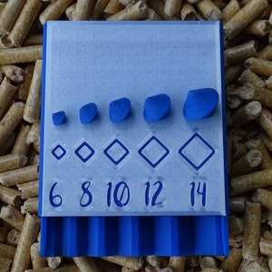 May include: A blue 3D-printed tool with a series of diamond shapes and blue pebble-like objects. The numbers 6, 8, 10, 12, and 14 are printed below the diamond shapes. The tool is set against a background of wood pellets.
