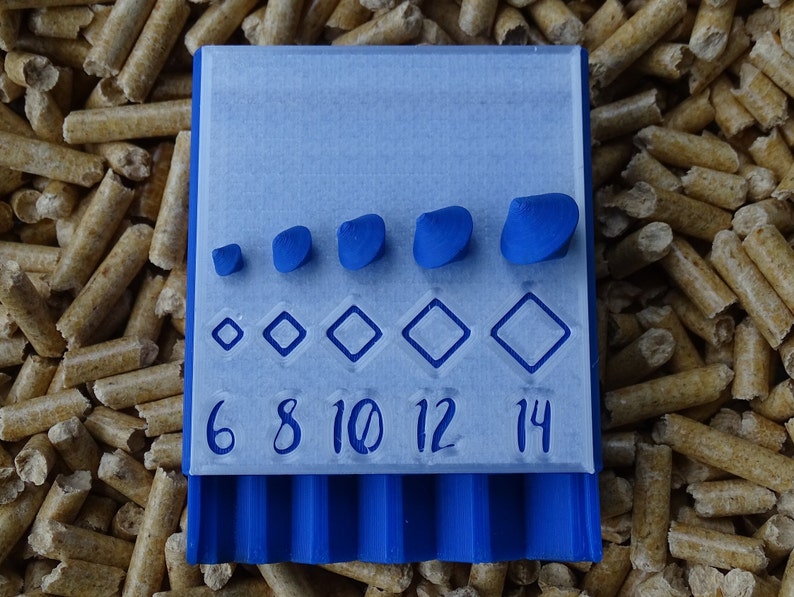 May include: A blue 3D-printed tool with a series of diamond shapes and blue pebble-like objects. The numbers 6, 8, 10, 12, and 14 are printed below the diamond shapes. The tool is set against a background of wood pellets.