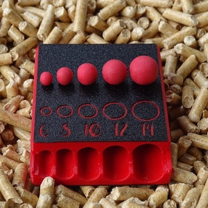 May include: A red and black tool with several red spheres of varying sizes. The tool has a black surface with numbered holes and a red base. The spheres are arranged in a row above the holes.