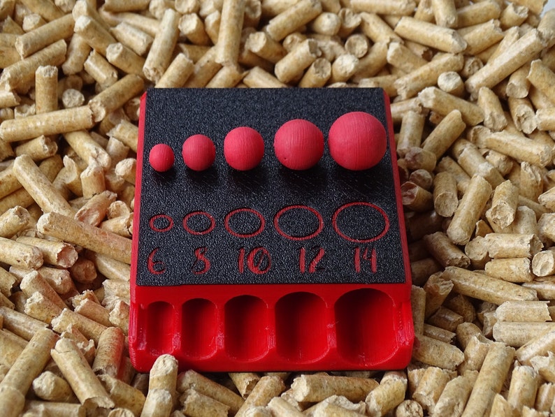 May include: A red and black tool with several red spheres of varying sizes. The tool has a black surface with numbered holes and a red base. The spheres are arranged in a row above the holes.