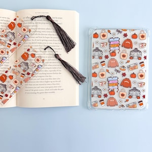 May include: Two clear rectangular bookmarks with dark brown tassels and a matching clear tablet case, all featuring a repeating autumn-themed pattern of orange pumpkins, brown sweaters, coffee cups, gazebos, and signs labeled Yale and Antiques.