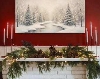May include: A winter landscape painting depicts a snowy forest scene with a river. The painting hangs above a white brick fireplace decorated with pine garland, pine cones, and string lights. Tall white candles in black holders flank the painting.