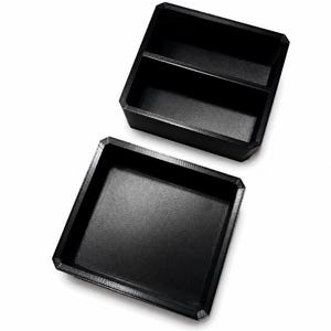 May include: A black storage box in two parts, with a textured surface. The top section is divided into two compartments. The bottom section is a single tray. The box is made of a matte black material.