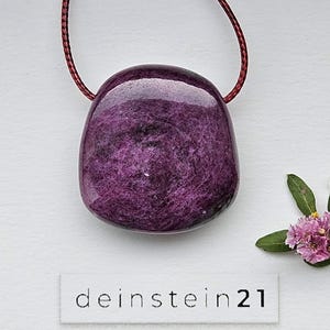 Peut inclure: Un pendentif en pierre polie, de forme arrondie et de couleur violette profonde, suspendu à un cordon fin rouge foncé. La pierre présente une surface texturée et marbrée avec des inclusions sombres. Une étiquette affiche "deinstein21".