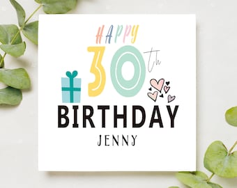 Puede incluir: Una tarjeta blanca con un mensaje de Feliz cumpleaños número 30 colorido con una caja de regalo, un número 30 grande y corazones. El nombre Jenny está impreso debajo del mensaje.