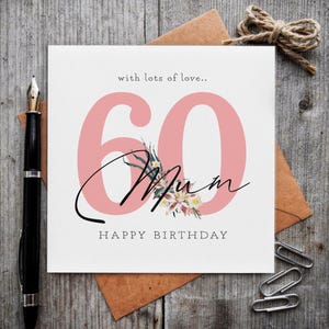 K&ouml;nnte beinhalten: Eine quadratische Gru&szlig;karte mit der gro&szlig;en rosa Zahl 60, dem schwarzen kursiven Schriftzug Mum und dem gedruckten Text with lots of love.. sowie HAPPY BIRTHDAY. Eine kleine Blumenillustration ist mittig &uuml;ber der Zahl 60 auf der wei&szlig;en Karte.