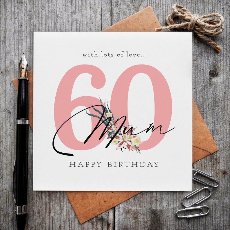 K&ouml;nnte beinhalten: Eine quadratische Gru&szlig;karte mit der gro&szlig;en rosa Zahl 60, dem schwarzen kursiven Schriftzug Mum und dem gedruckten Text with lots of love.. sowie HAPPY BIRTHDAY. Eine kleine Blumenillustration ist mittig &uuml;ber der Zahl 60 auf der wei&szlig;en Karte.