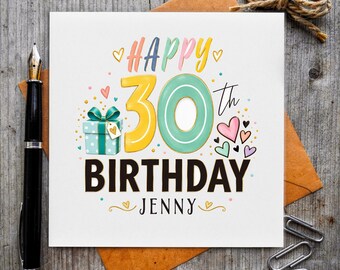 May include: A square greeting card featuring the text Happy 30th Birthday Jenny in colorful lettering. The design includes a light blue gift box with a bow, various small hearts, and gold dots on a white background, accompanied by a black fountain pen.