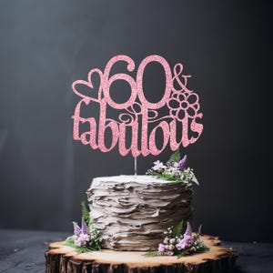 A cake with a pink glittery topper that says "60 & fabulous" and is surrounded by purple flowers.