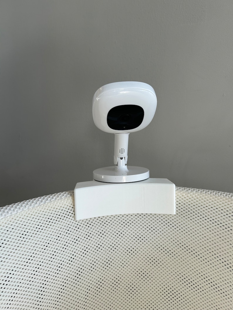 May include: White baby monitor camera mounted on a white mesh bassinet.