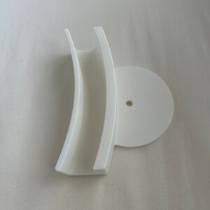 May include: White plastic wall mount with a curved, open-ended slot and a round base with a small hole in the center.