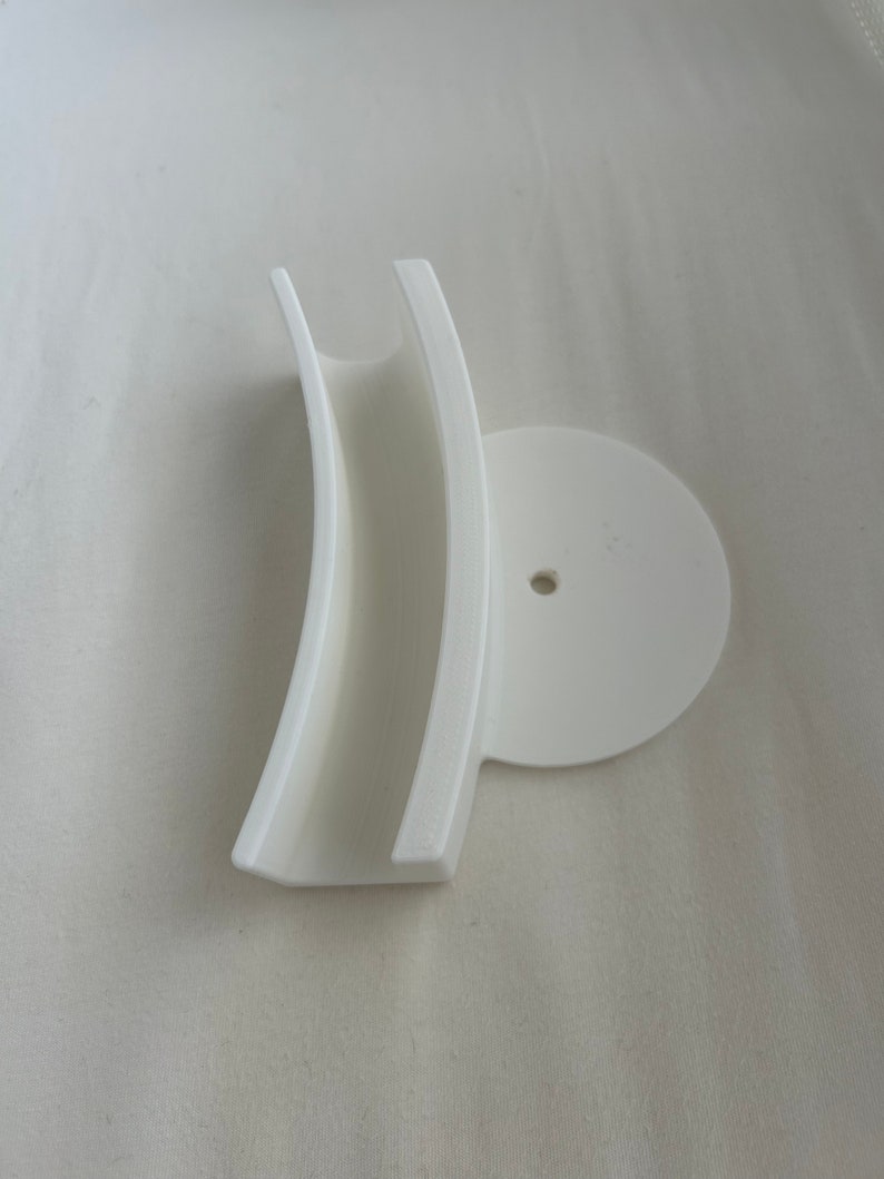 May include: White plastic wall mount with a curved, open-ended slot and a round base with a small hole in the center.
