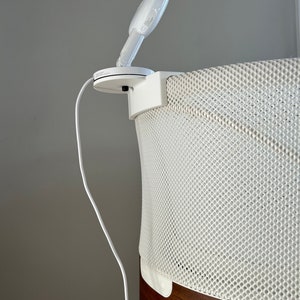 May include: A white baby monitor with a white cord attached to it is mounted on a white mesh bassinet with a brown wooden base.