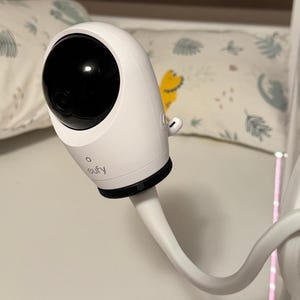 Può includere: Una telecamera di sicurezza Eufy bianca con alloggiamento dell'obiettivo circolare nero, montata su un braccio bianco flessibile. Il dispositivo presenta un esterno liscio e arrotondato, una piccola spia sotto l'obiettivo e una porta laterale.
