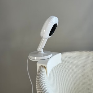 May include: White baby monitor camera mounted on a white crib with a white mesh design.