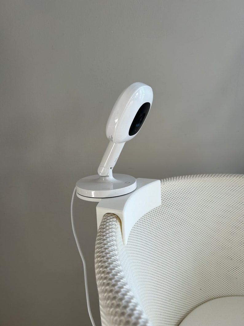 May include: White baby monitor camera mounted on a white crib with a white mesh design.