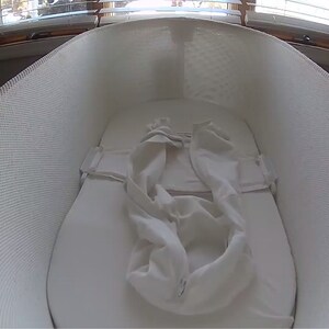 May include: A white mesh bassinet with a white fitted sheet and a white blanket inside. The bassinet is made by the company "nanit".