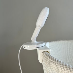 May include: White baby monitor with a round camera lens mounted on a white crib with a mesh side.