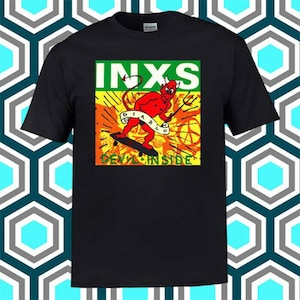 Puede incluir: Camiseta negra con un estampado gráfico de un diablo rojo en un monopatín. El gráfico incluye el texto "INXS" y "DEVIL INSIDE".