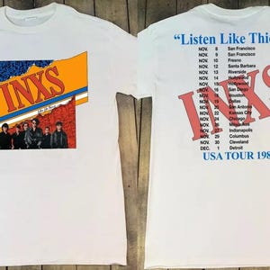 May include: White t-shirt with a red, orange, and blue graphic of the band INXS on the front. The back of the shirt has a red graphic of INXS with the text "Listen Like Thieves" and a list of tour dates for the USA in 1985.