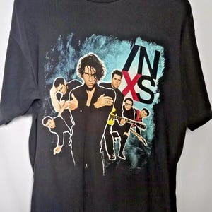 May include: Black t-shirt with a graphic print of the band INXS. The band members are depicted in a stylized, colorful design against a blue and white background.