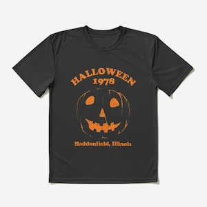Puede incluir: Camiseta negra con un gráfico naranja de una calabaza y el texto "Halloween 1978 Haddonfield, Illinois".