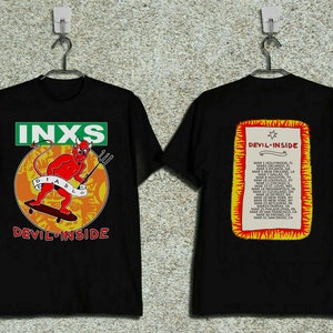 May include: Black t-shirt featuring a red devil on a skateboard with the text "INXS Devil Inside". The back of the shirt displays a white rectangle with the text "Devil Inside" and a list of cities and dates.