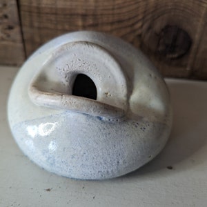 May include: A white ceramic object with a blue glaze. The object has a hole in the center and a raised lip around the opening.