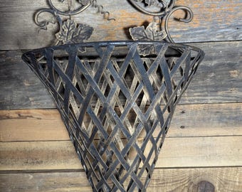 May include: A wall-mounted metal basket with a triangular, lattice-style design. The basket features a dark finish with gold-toned highlights and is decorated with metal grape leaves and vine tendrils at the top, including a small circular hanging loop.