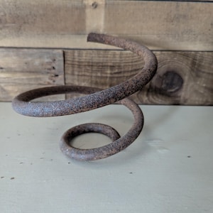 May include: A rusty metal spring, coiled in a spiral shape. The spring is a dark brown color with areas of rust.