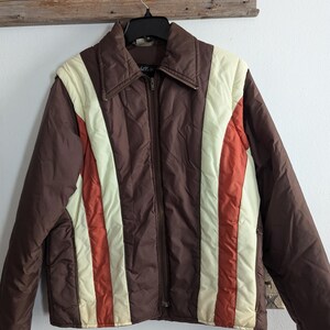 May include: A brown puffer jacket with vertical stripes of white and orange. The jacket has a zipper closure and a stand-up collar.