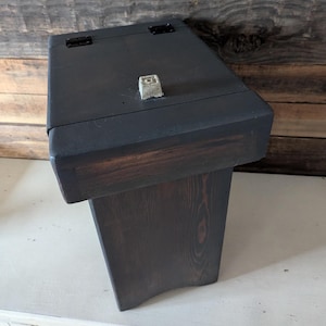 May include: A dark wooden box with a hinged lid and a small metal latch. The box is made of dark wood with a natural grain pattern. The box is closed and sitting on a white surface.