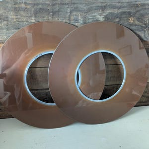 May include: Two brown, circular objects with a white inner ring. The objects are overlapping, and the text "BN455" is visible on one. The objects are set against a weathered wood background.