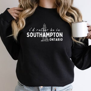 Könnte beinhalten: Schwarzer Pullover mit einem weißen Grafikdruck eines Leuchtturms und dem Text "i'd rather be in SOUTHAMPTON ONTARIO".