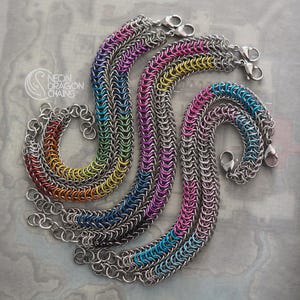 May include: Three chainmail bracelets featuring interlocking metal rings. One bracelet displays a full rainbow gradient, another shows a purple and blue pattern, and the third features pink and blue rings. Each includes a silver lobster clasp.
