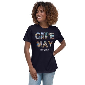 May include: A navy blue t-shirt with a graphic of the words "CAPE MAY" in white letters. The letters are made up of images of the town of Cape May, New Jersey. The text "NEW JERSEY" is printed in white below the graphic.
