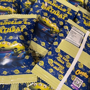 May include: A stack of small blue and yellow bags with a cartoon alien character on the front. The bags are labeled "Dangelo's Birthday" and have a Cheeto's logo on the side.
