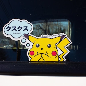 May include: A yellow Pikachu sticker with a thought bubble that says "クスクス (giggles)" in Japanese. The sticker has a black border and is on a car window. The sticker also has the text "@carnivore_motorsports".
