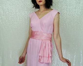 May include: A pink sleeveless dress with a matching pink sash tied in a bow at the waist. The dress has a v-neckline and a fitted bodice.