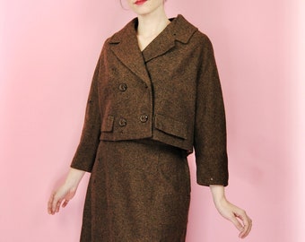 May include: A brown tweed skirt suit with a cropped jacket featuring a double-breasted closure and flap pockets. The jacket has three buttons and the skirt is knee-length.