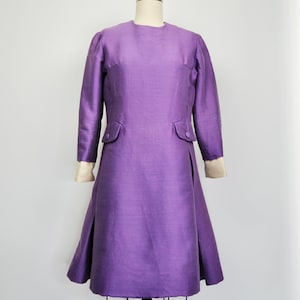 May include: A purple dress with long sleeves and a fitted bodice. The dress has a slight A-line shape and a simple, elegant design.