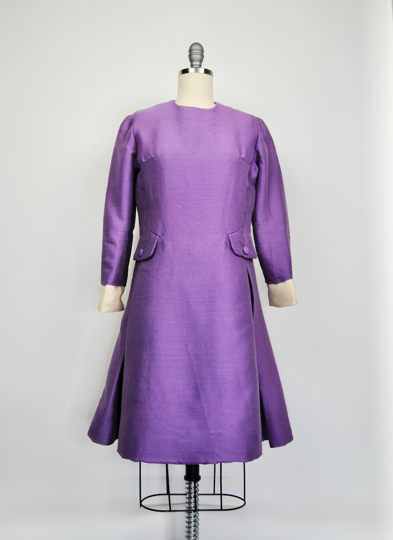 May include: A purple dress with long sleeves and a fitted bodice. The dress has a slight A-line shape and a simple, elegant design.