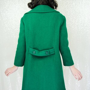 Pu&ograve; includere: Un lungo cappotto di lana verde con chiusura a doppio petto e due bottoni sul retro.