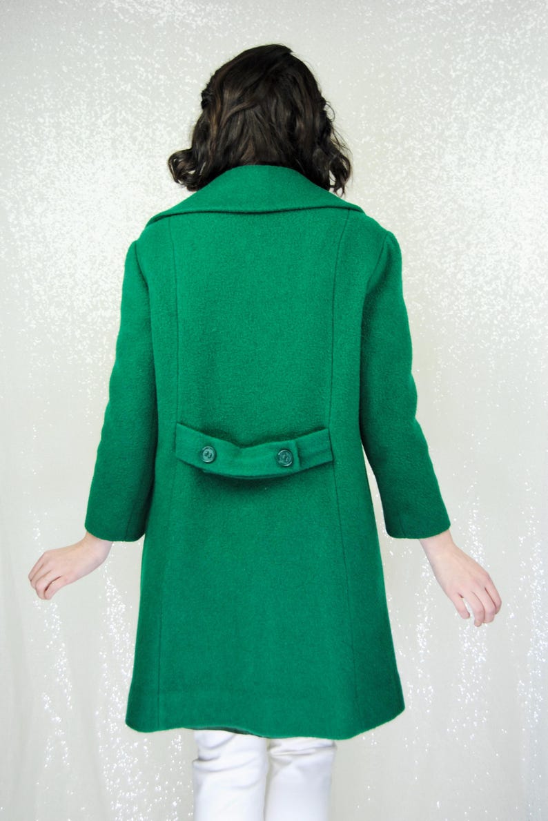 Pu&ograve; includere: Un lungo cappotto di lana verde con chiusura a doppio petto e due bottoni sul retro.