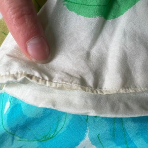 May include: Close-up of a white fabric with a green and blue floral pattern. The fabric has a subtle sheen and a delicate texture.