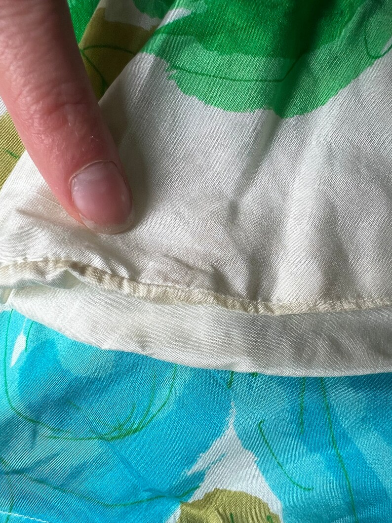 May include: Close-up of a white fabric with a green and blue floral pattern. The fabric has a subtle sheen and a delicate texture.