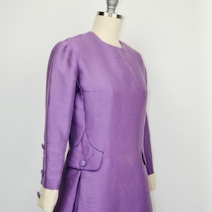 May include: A long-sleeved, purple dress with a round neckline and button details on the cuffs and pockets.